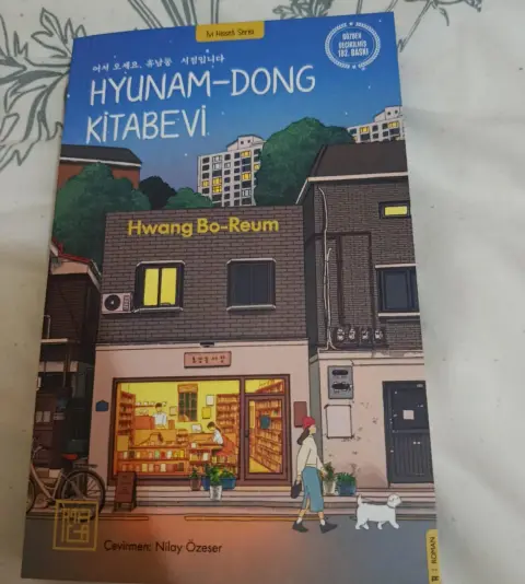 Hyunam-Dong Kitabevi kitabının kapağı: gece ışıkları yanan küçük bir kitabevi ve önünden köpeğiyle geçen bir kadın
